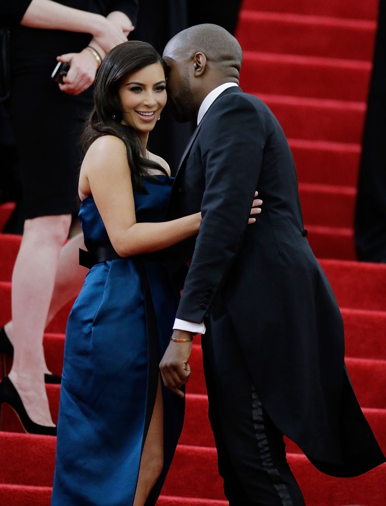 Kanye whispers into the ear of a smiling Kim Kardashian on the 2014 Met Gala red carpet.