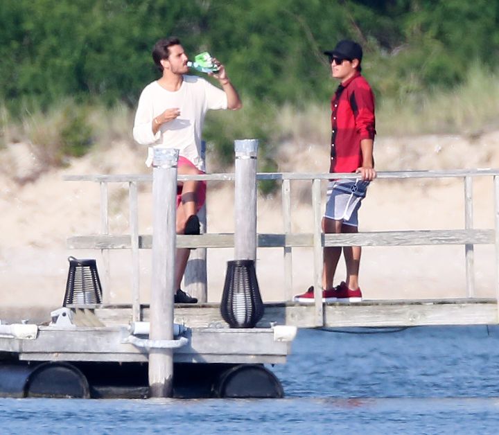 Scott Disick chows down on chips and drink while showing a friend the view from the pier of his house in the Hamptons, NY.