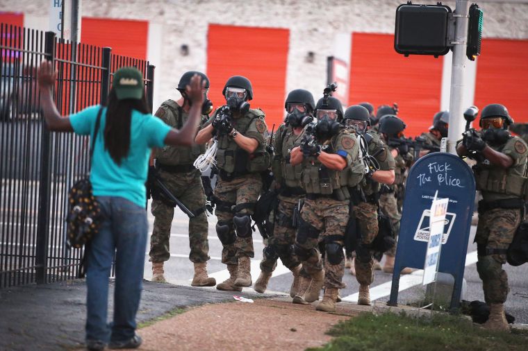 Police carrying rifles in riot gear approach a young unarmed man in Ferguson.