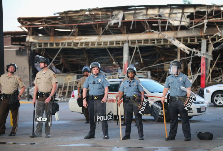 Police in riot gear and sticks stand guard at a store destroyed in Ferguson riots.