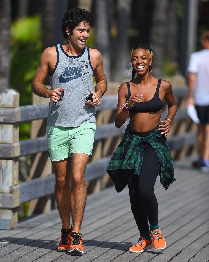 Adrian Grenier, wearing orange sneakers and a Nike tank top, runs with a mystery woman and is seen having a laugh while on the boardwalk in Miami Beach, Florida.