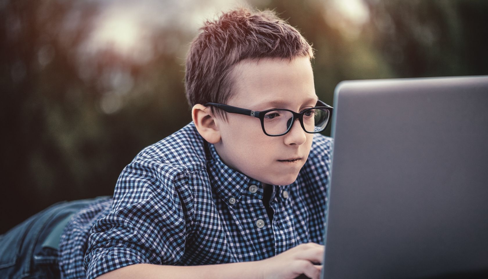 Boy using a laptop lying on wooden pier at sunset
