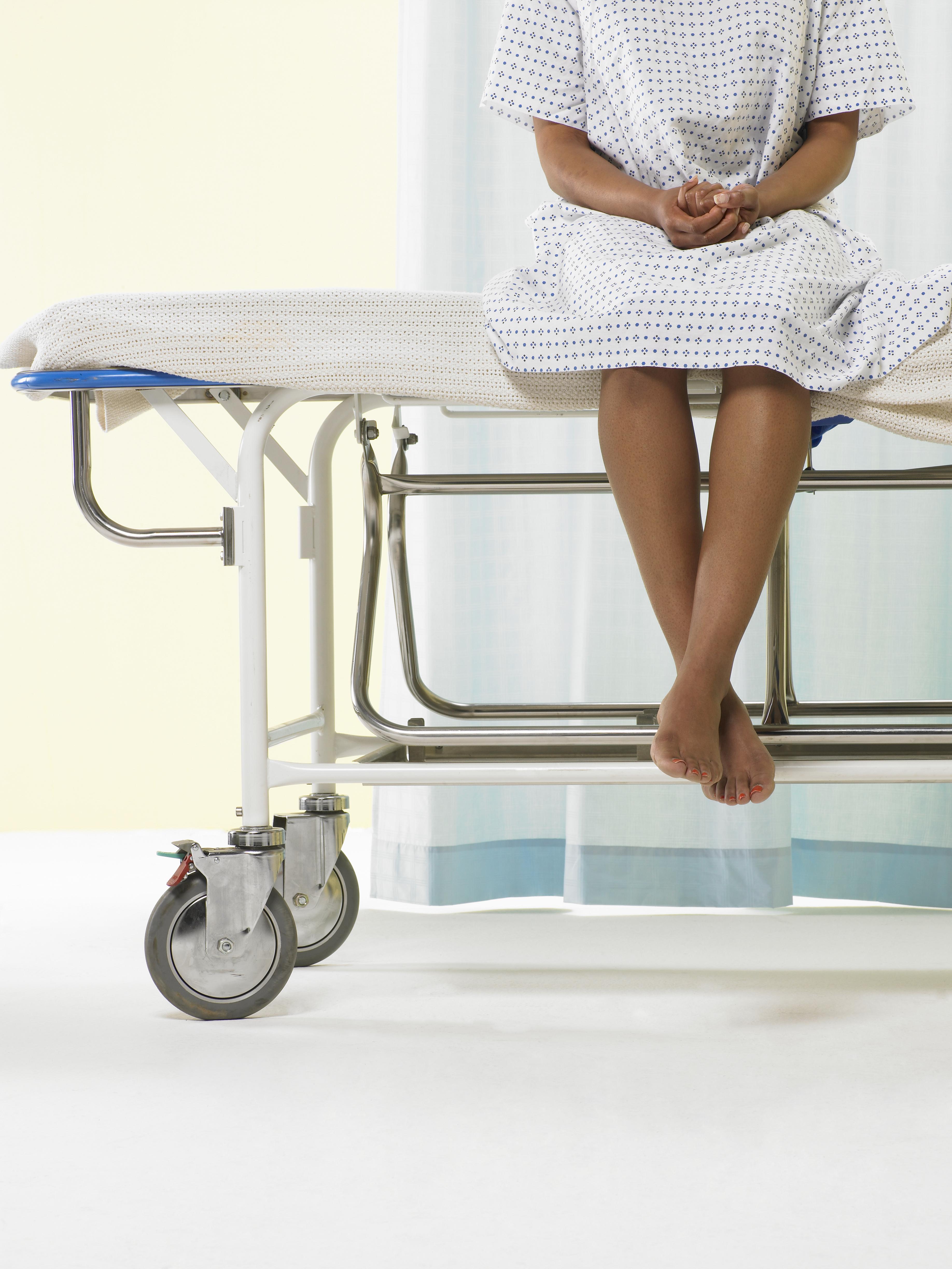 Female patient sitting on gurney in hospital gown, low section