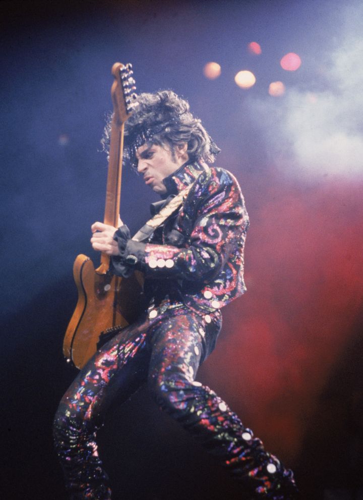 Prince plays guitar on stage during a concert, 1985.
