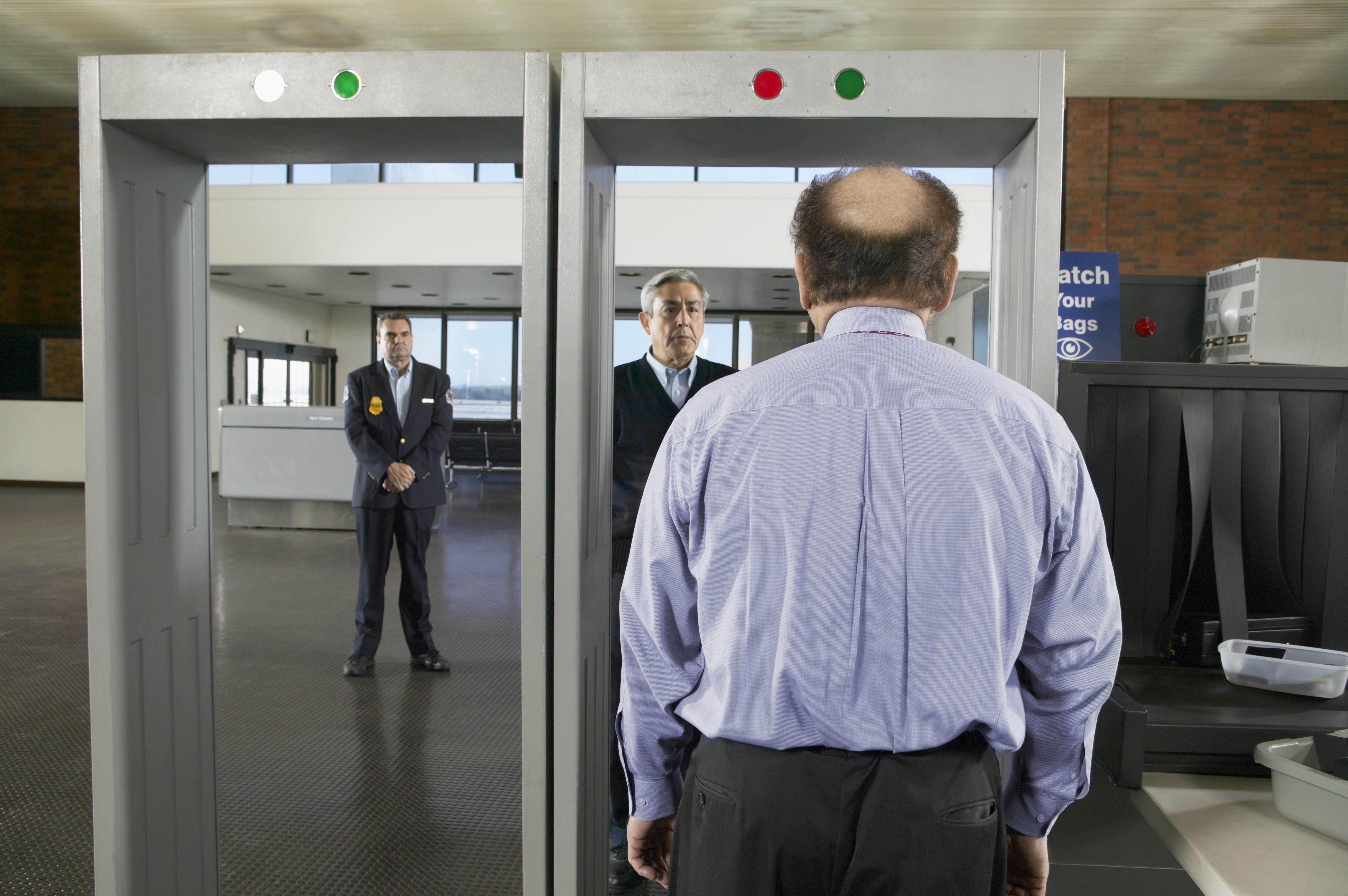 Rear View of a Balding Man Walking Through an Airport Metal Detector