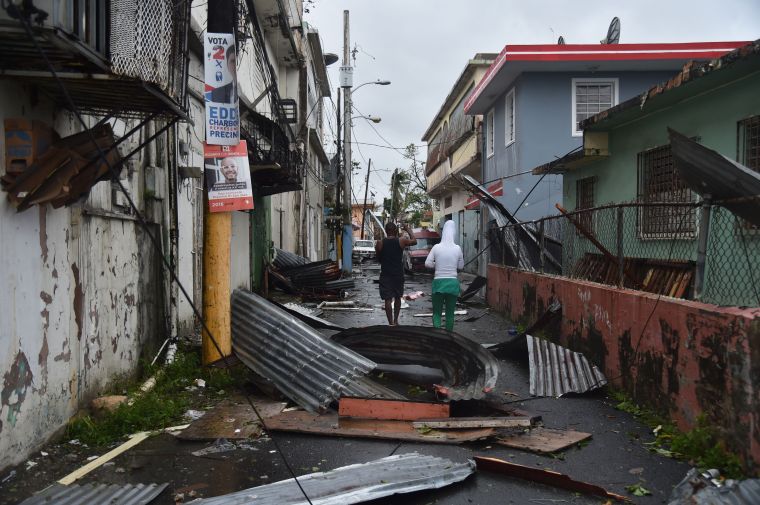 San Juan, PR: Residents walk past damaged homes following Hurricane Maria.