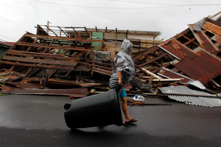 Fajardo, PR: A woman pulls a trash can past a destroyed home.