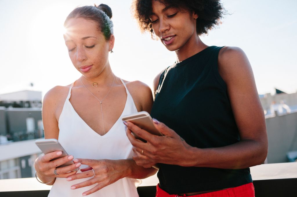 Female friends standing on rooftop using their smart phones