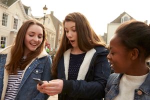 Teenage Girls Walking Along Street Looking At Social Media