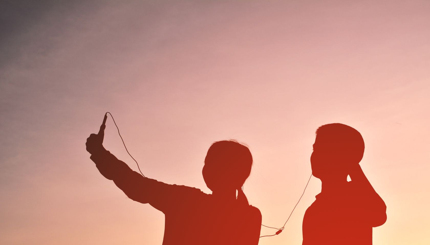 Silhouette Friends Taking Selfie While Listening Music Through Headphones Against Sky During Sunset