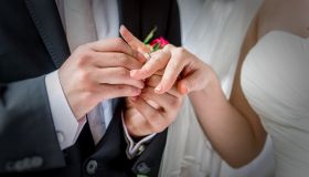Midsection Of Groom Putting Ring In Bride Finger At Wedding