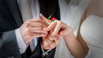 Midsection Of Groom Putting Ring In Bride Finger At Wedding