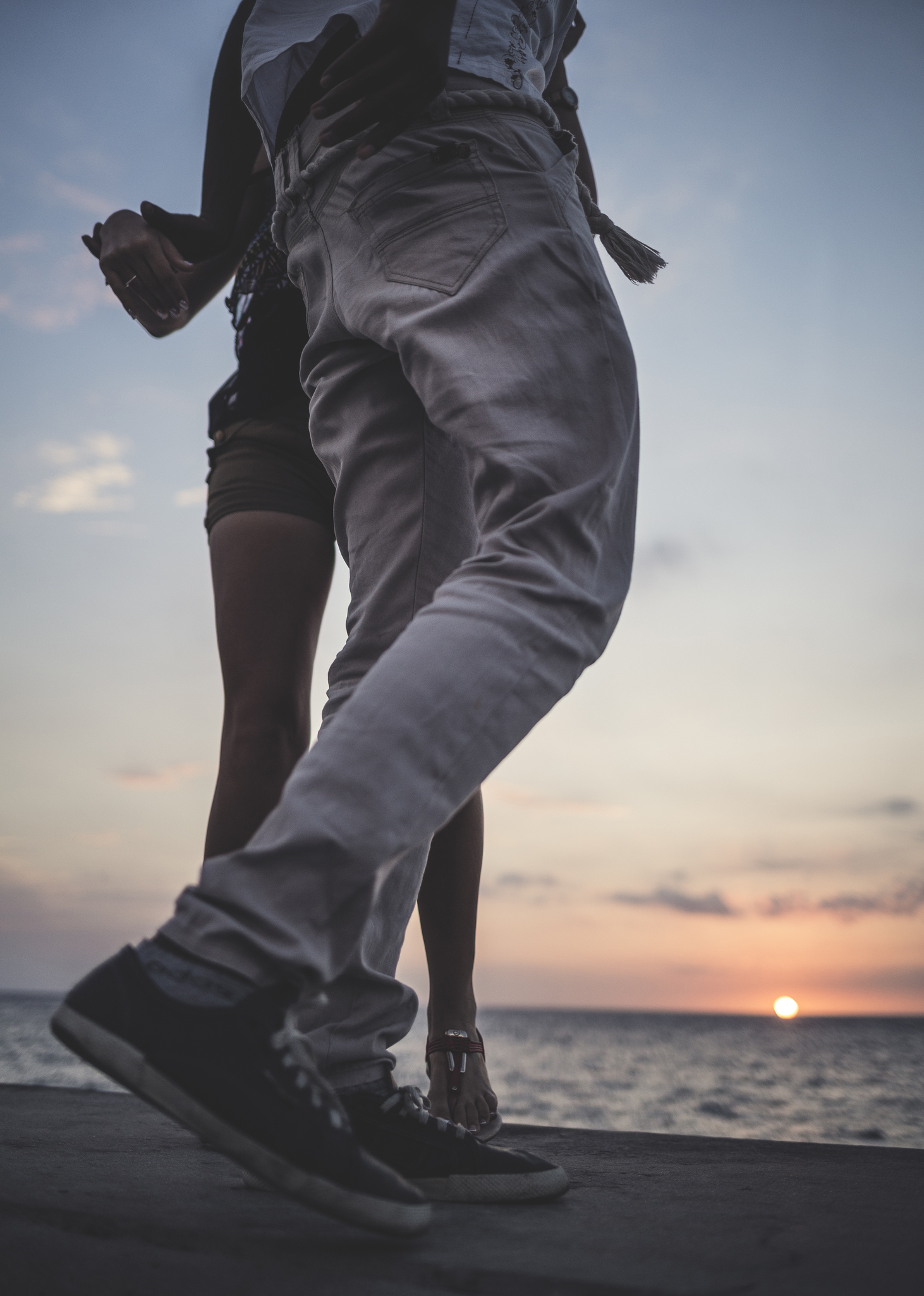 Low angle shot of two people dancing on a sea wall in front of the ocean.