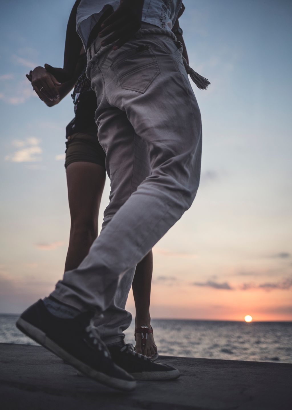 Low angle shot of two people dancing on a sea wall in front of the ocean.
