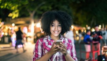 Smiling woman using smart phone on street at night
