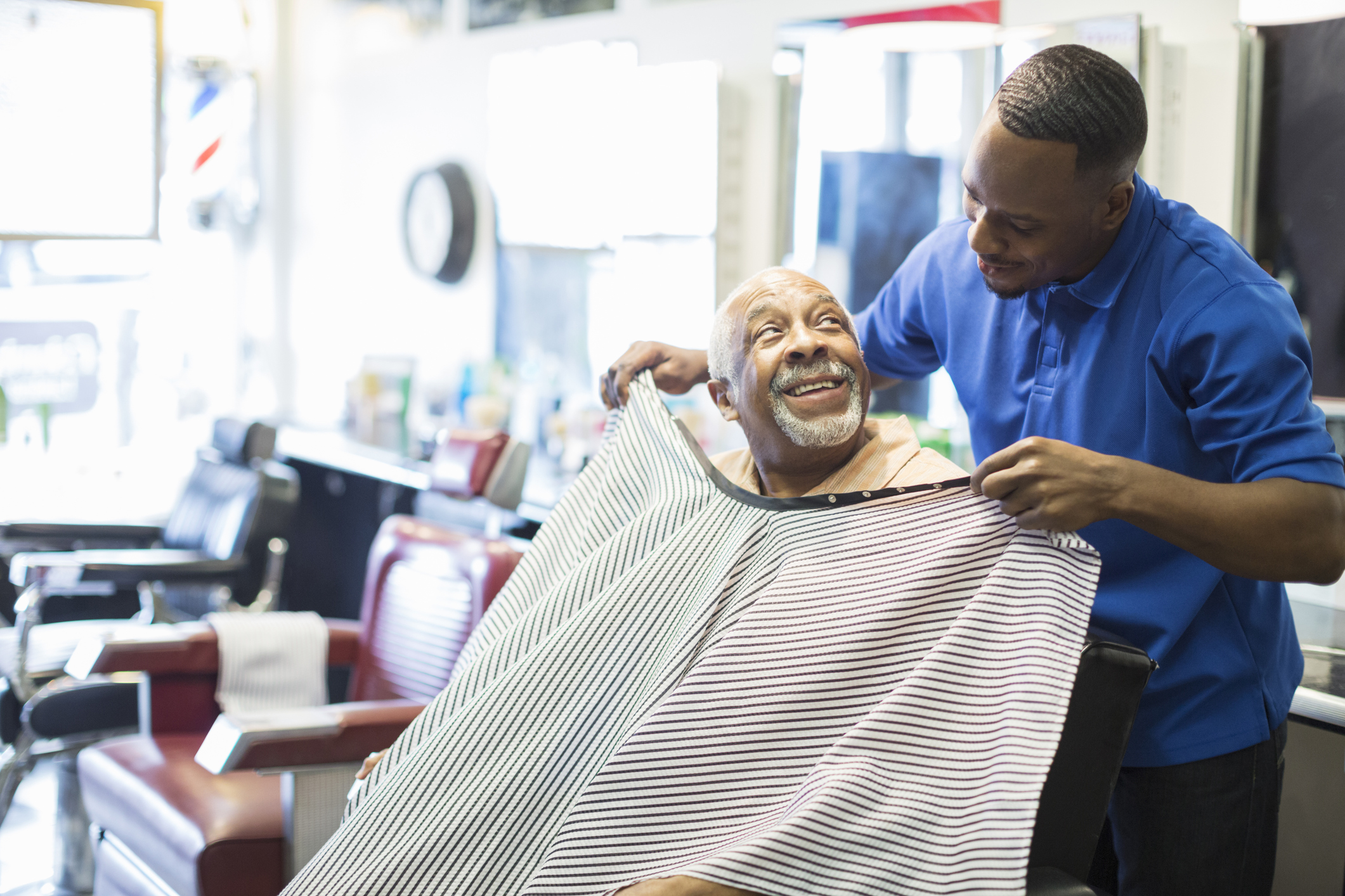 Black barber tying apron on customer in retro barbershop