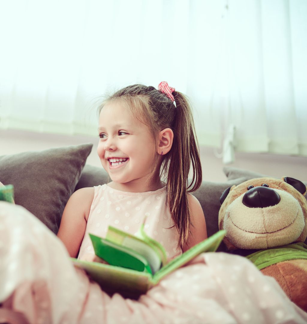 Smiling Toddler Girl Reading Book To Toy Bear