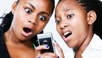 Two young women look down, horrified, at mobile phone