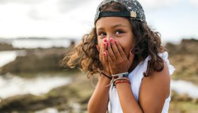 Spain, Gijon, portrait of little girl covering mouth with her hands
