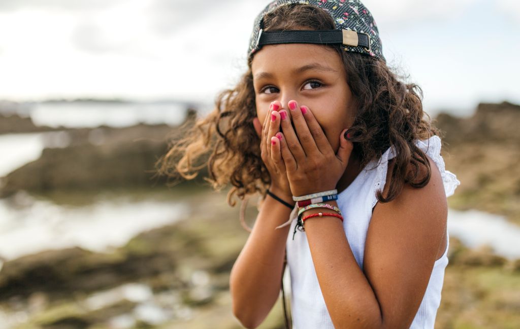 Spain, Gijon, portrait of little girl covering mouth with her hands