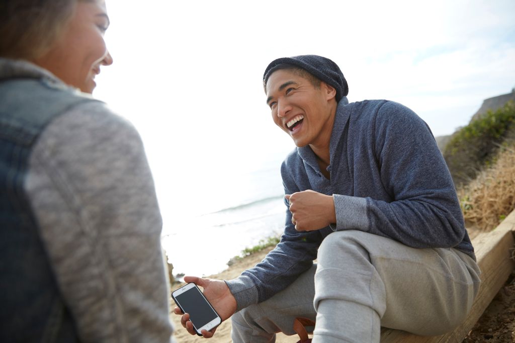 Man with smartphone laughing with friend by coast