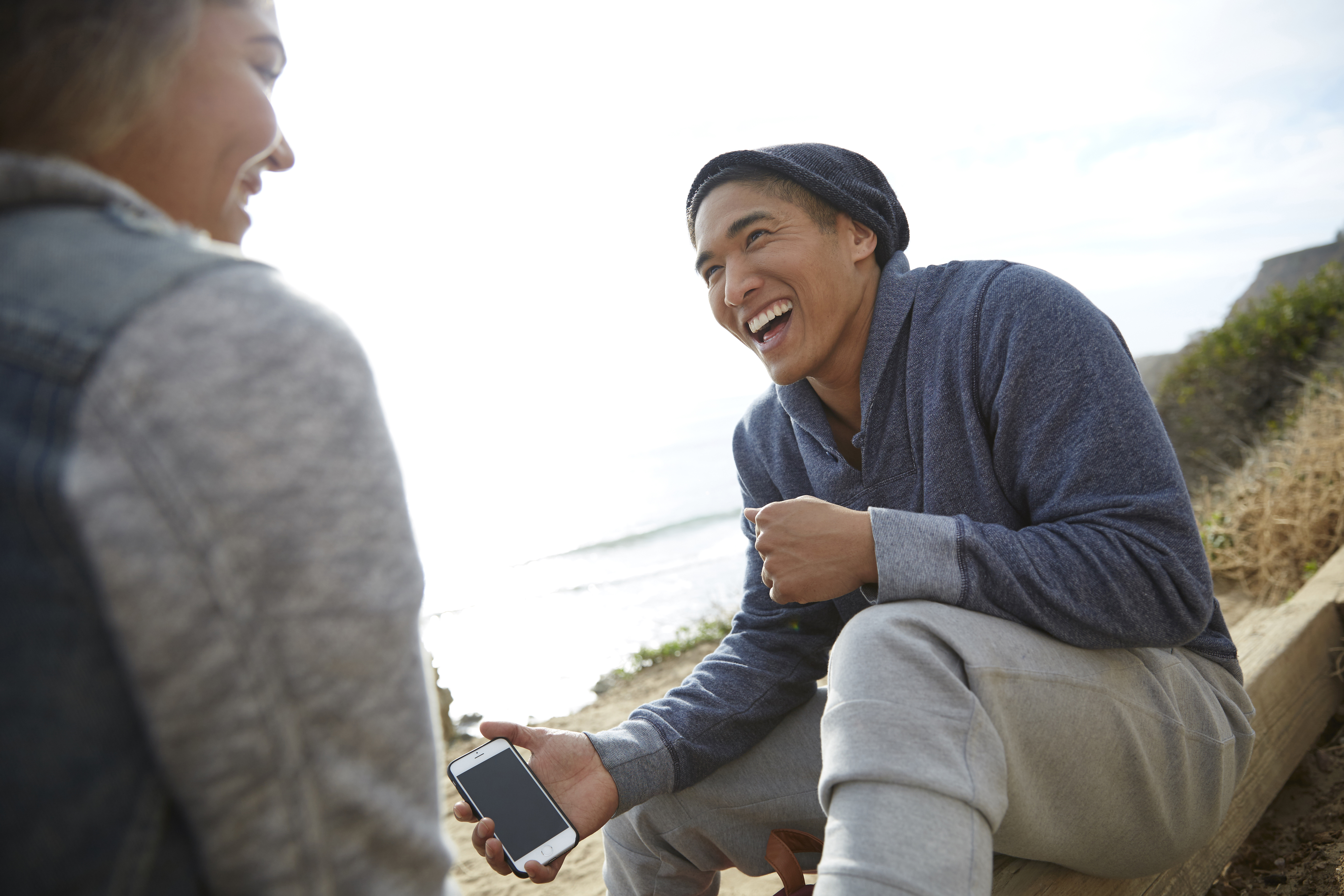 Man with smartphone laughing with friend by coast