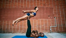 Couple performing acro yoga on sidewalk near brick wall