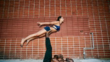 Couple performing acro yoga on sidewalk near brick wall