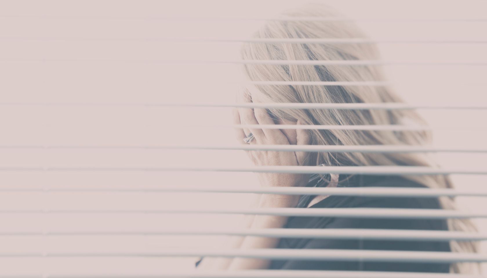 Woman With Blond Hair Seen Hiding Her Face Through A Window With Blinds