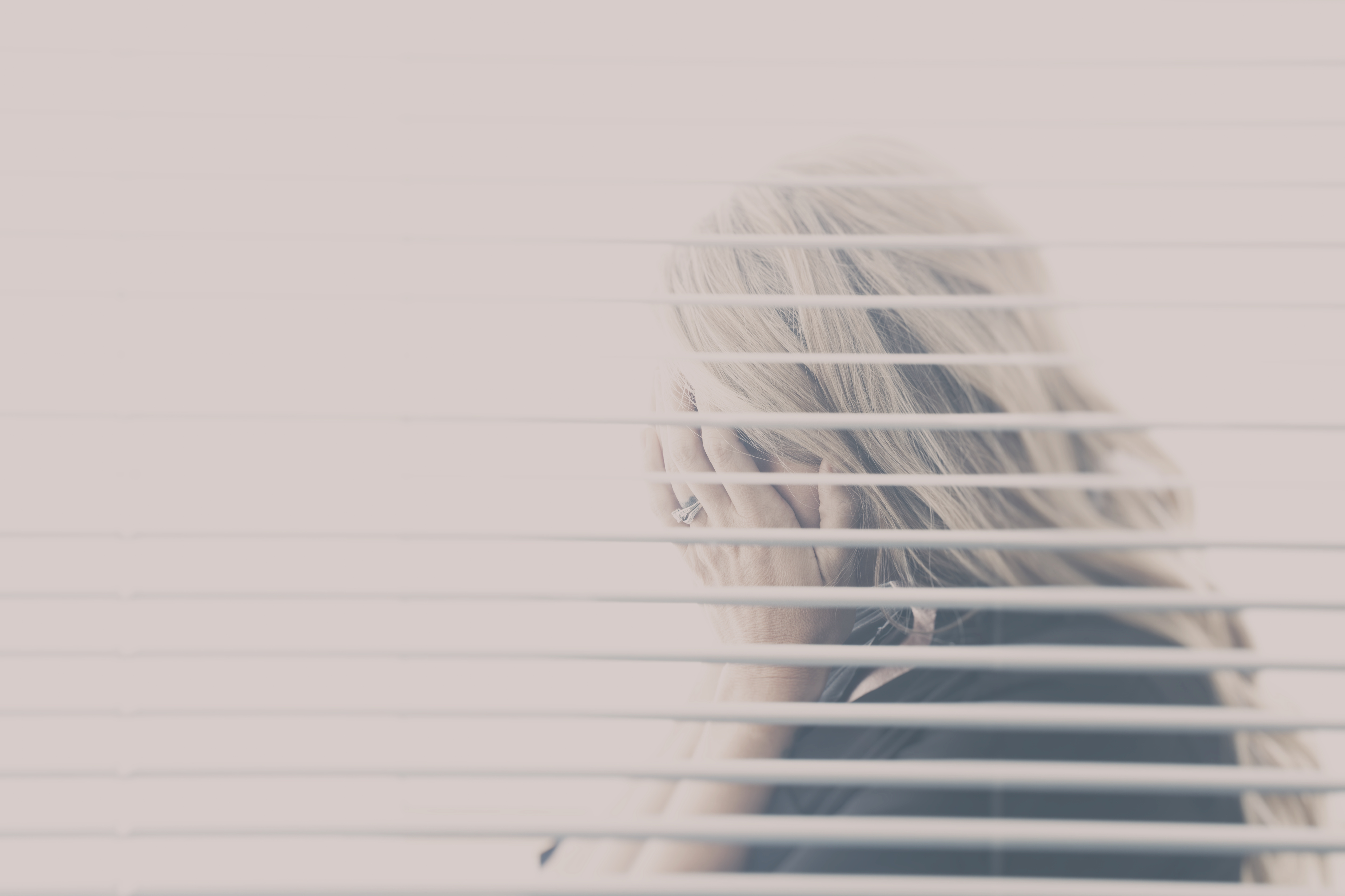 Woman With Blond Hair Seen Hiding Her Face Through A Window With Blinds