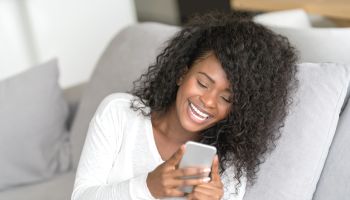 Beautiful female black woman chatting on her smartphone laughing while relaxing at home
