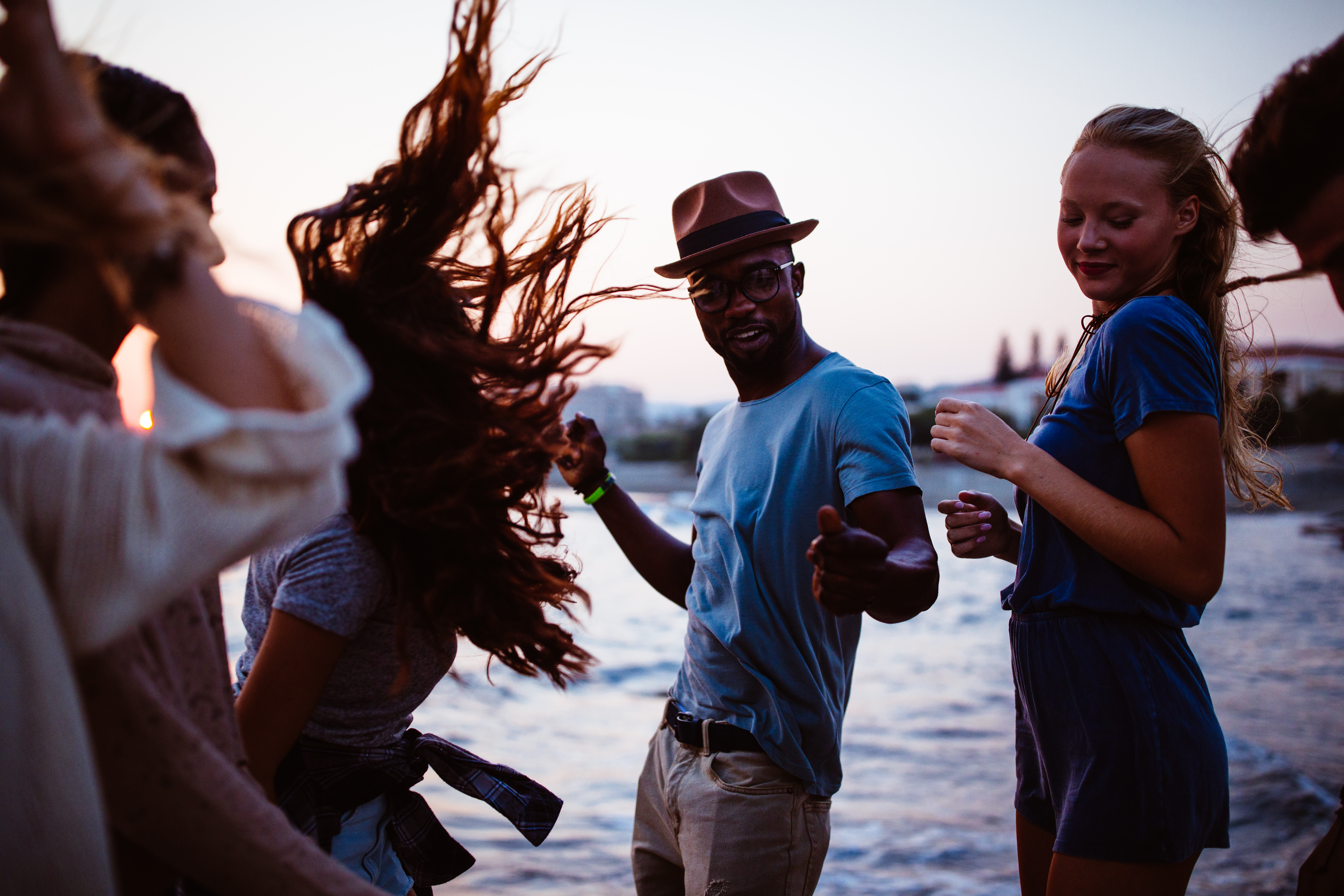 Young multi-ethnic hipster friends dancing at beach party at sunset