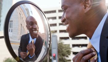 African American businessman adjusting tie in mirror