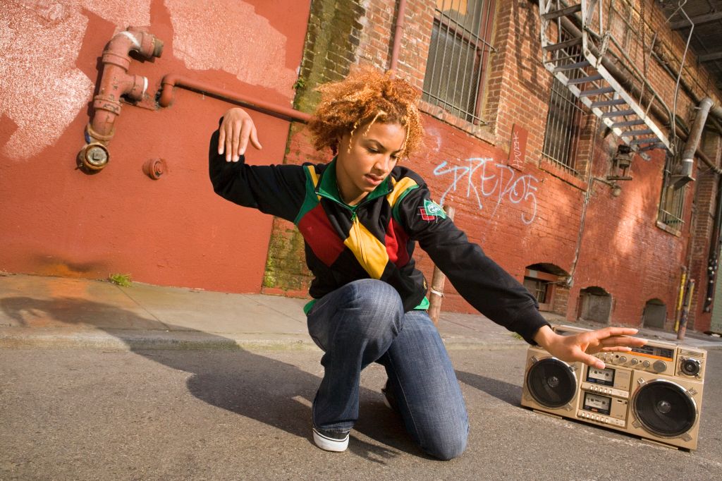 Young woman kneeling on street, dancing to stereo, low angle view