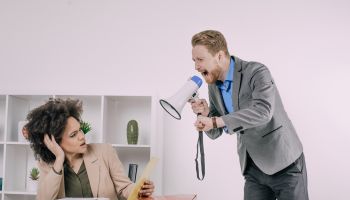 Business man screaming with megaphone at frustrated female coworker