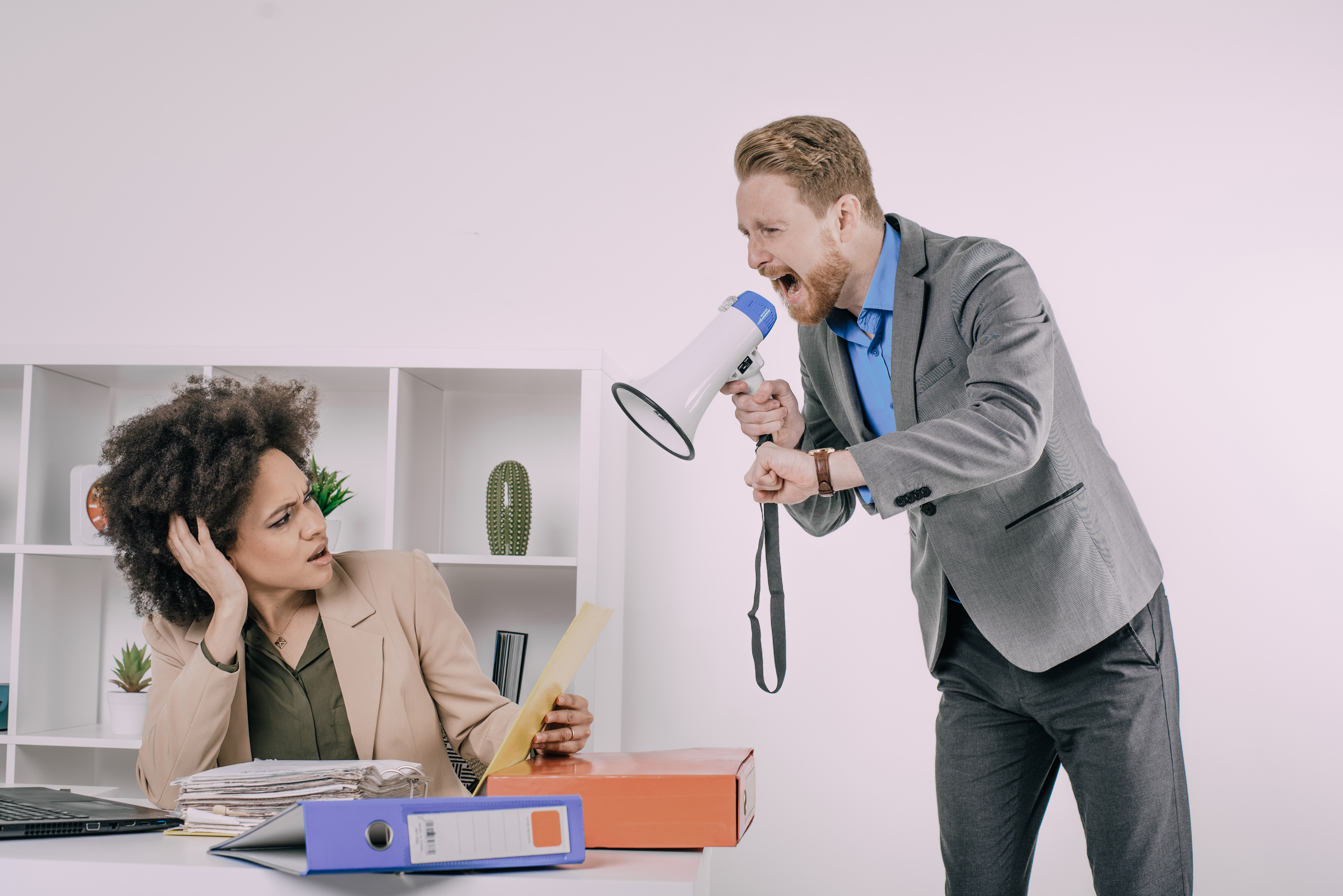 Business man screaming with megaphone at frustrated female coworker