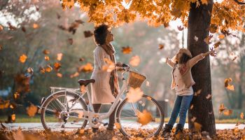 Carefree African American mother and daughter enjoying among autumn leaves at the park.