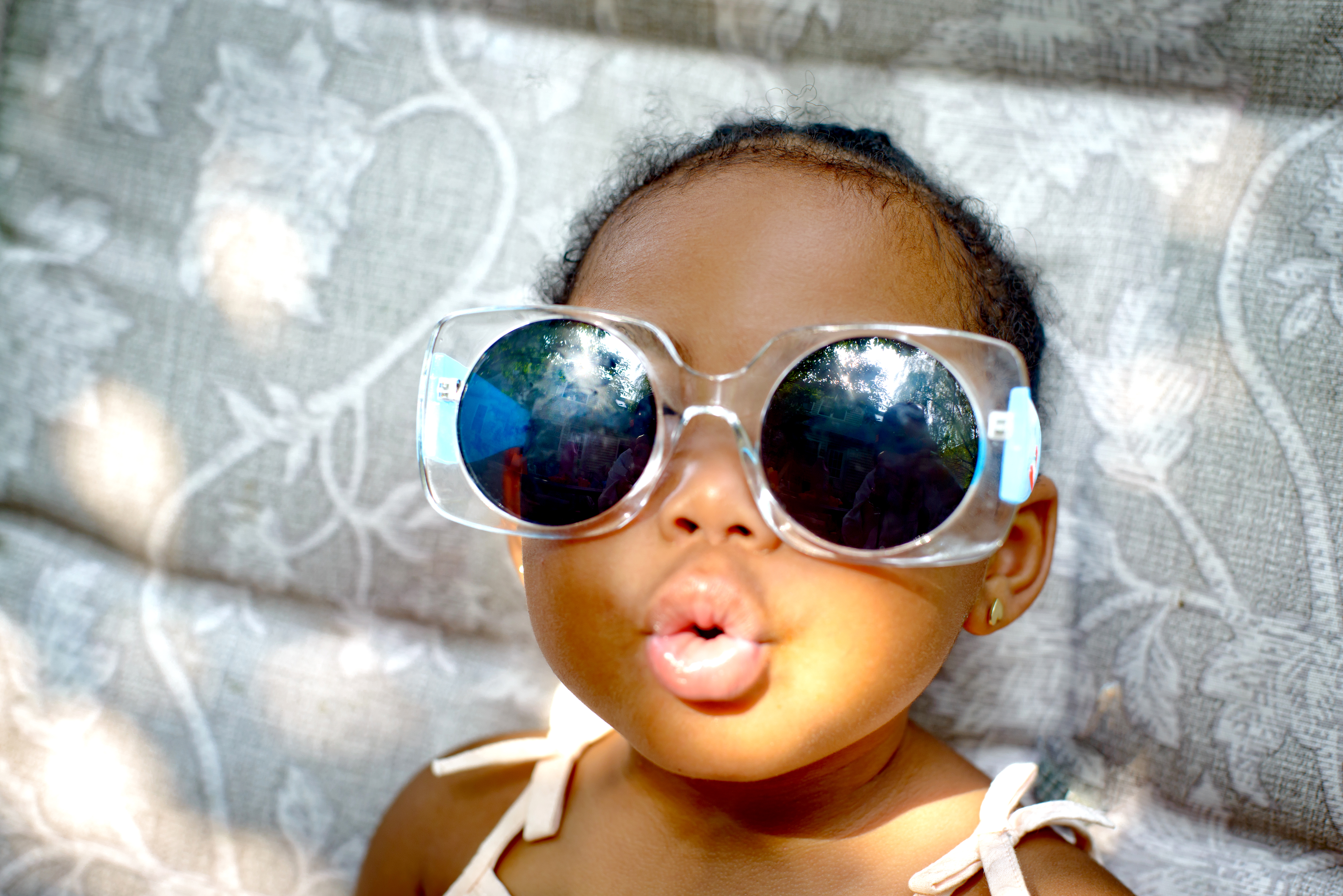 Baby girl sitting on lounge chair wearing sunglasses, portrait