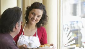 Young waitress serving client in cafe, smiling