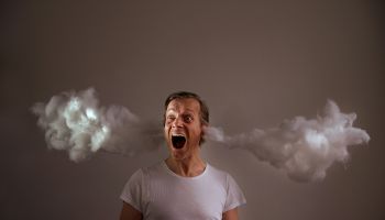 Screaming Man With Cotton Emitting From Ears Against Gray Background