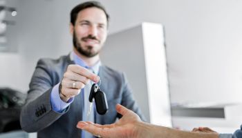 Car salesman making a sale in office delivering car key
