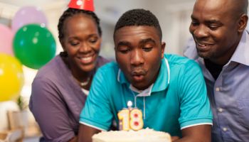 African male teenager blowing out the candles on his 18th birthday cake surrounded by his family , Cape Town, South Africa