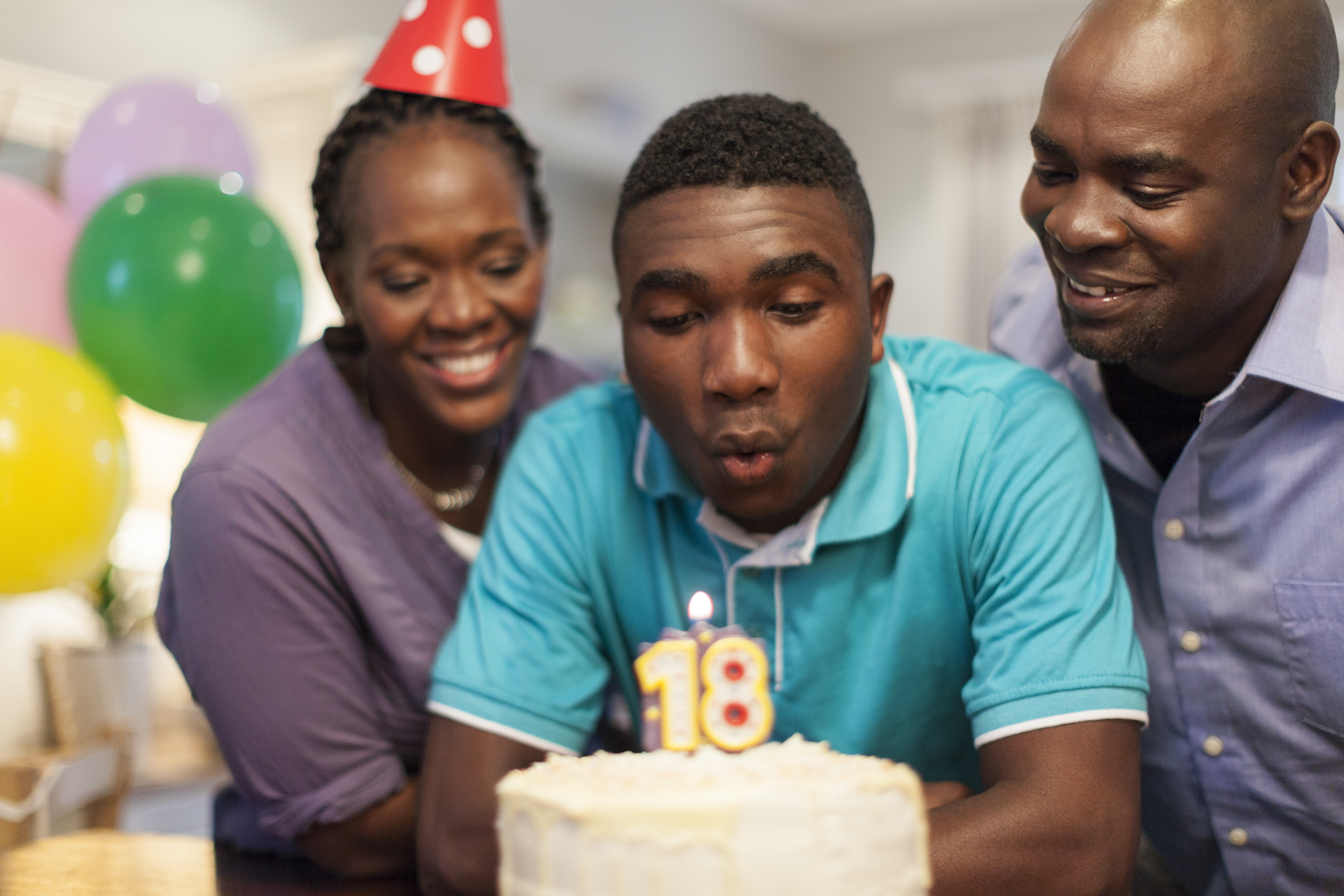 African male teenager blowing out the candles on his 18th birthday cake surrounded by his family , Cape Town, South Africa