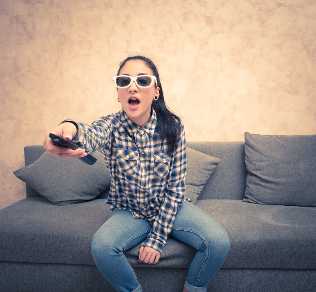 Young Woman Holding Remote Control While Sitting On Sofa At Home