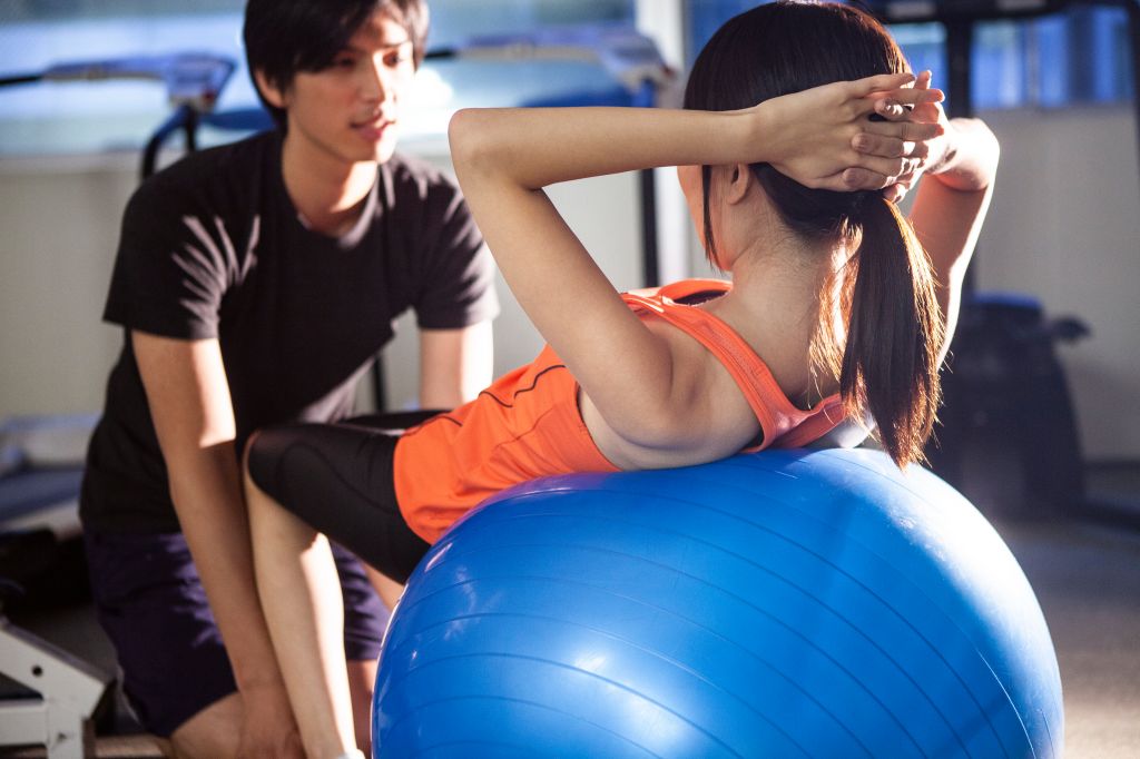 Man and woman working out with exercise ball in gym.