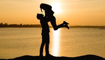 Silhouette Man Lifting Woman By Lake During Sunset