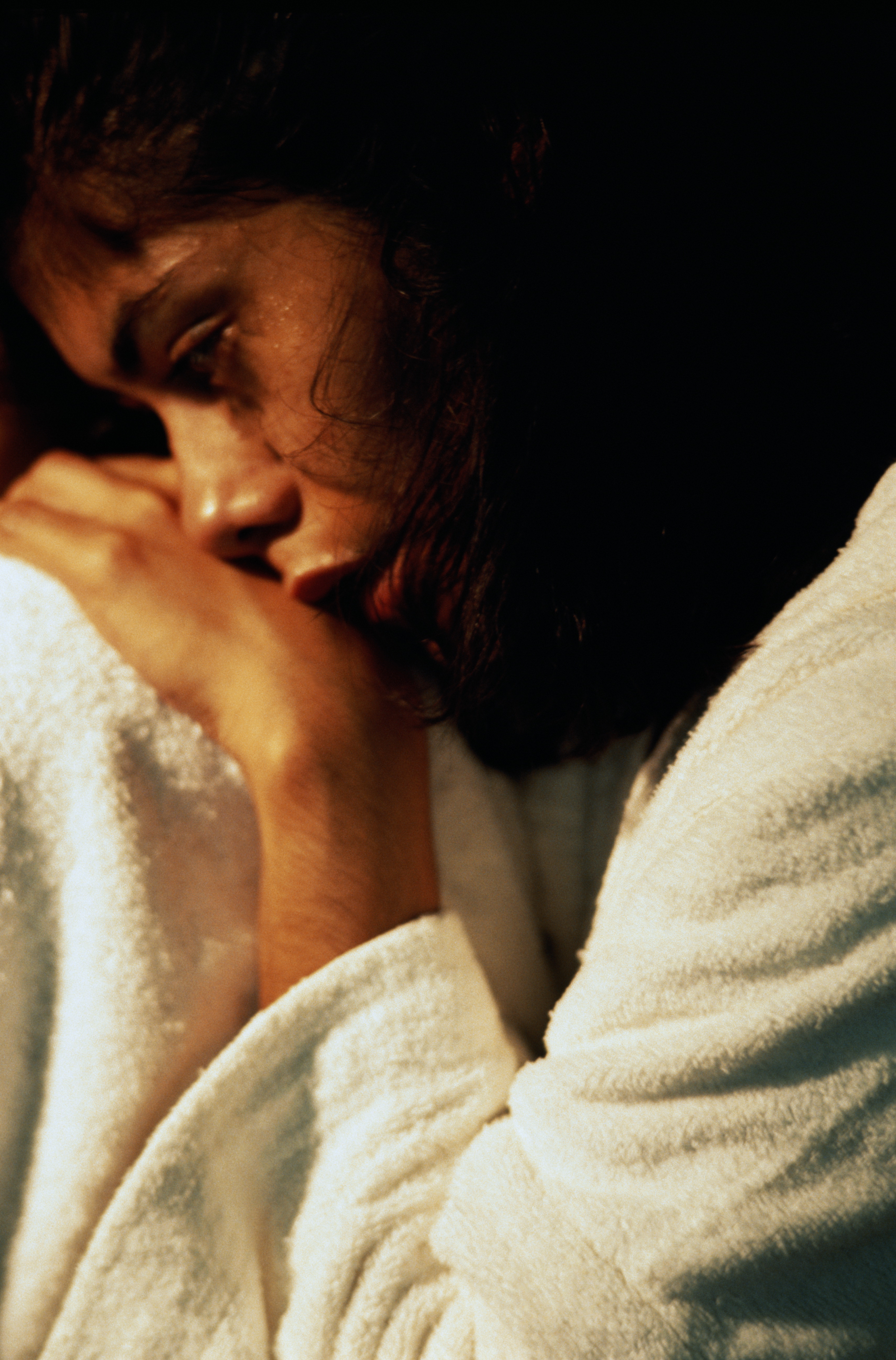 Woman in white bathrobe curled up and looking pensive