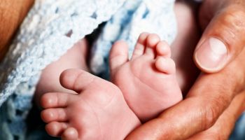Tiny baby feet cradled by huge hands of his father