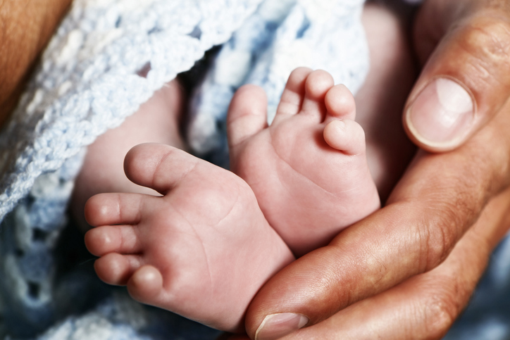 Tiny baby feet cradled by huge hands of his father