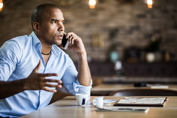 Black businessman arguing with someone over cell phone in a cafe.
